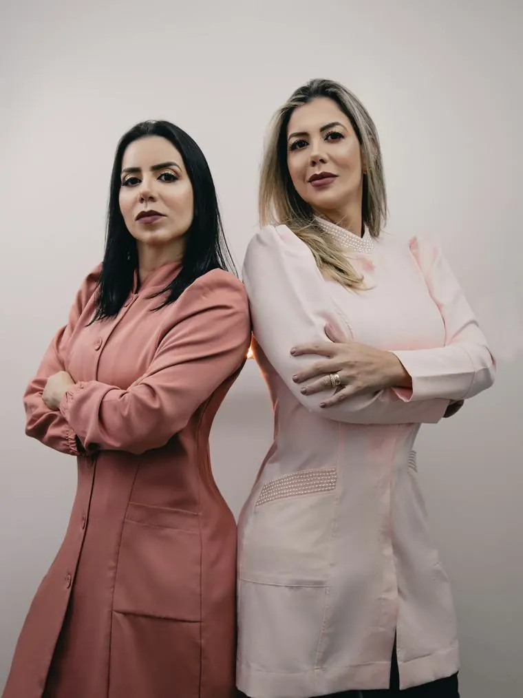 Las dos cosmiatras del centro, de espaldas una contra otra, con ambos de trabajo rosados