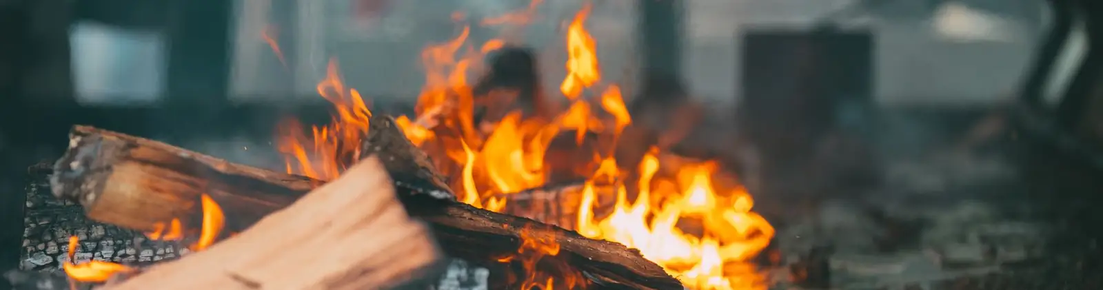 Leños partidos ardiendo en el asador de un campo, con las llamas saliendo de la leña y las cruces de hierro atrás