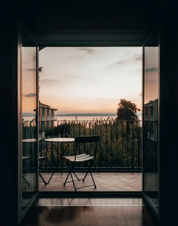 Puerta abierta a la galería de una habitación, con mesa y silla mirando al lago al atardecer