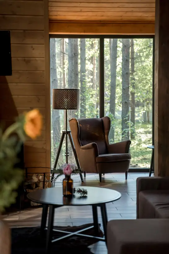 Estar de la cabaña con sillón, mesa baja y un ventanal de piso a techo hacia el bosque de pinos