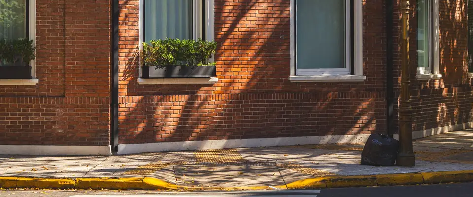 Esquina de una casa de ladrillo con la sombra de los árboles sobre la pared y el cordón amarillo de la vereda
