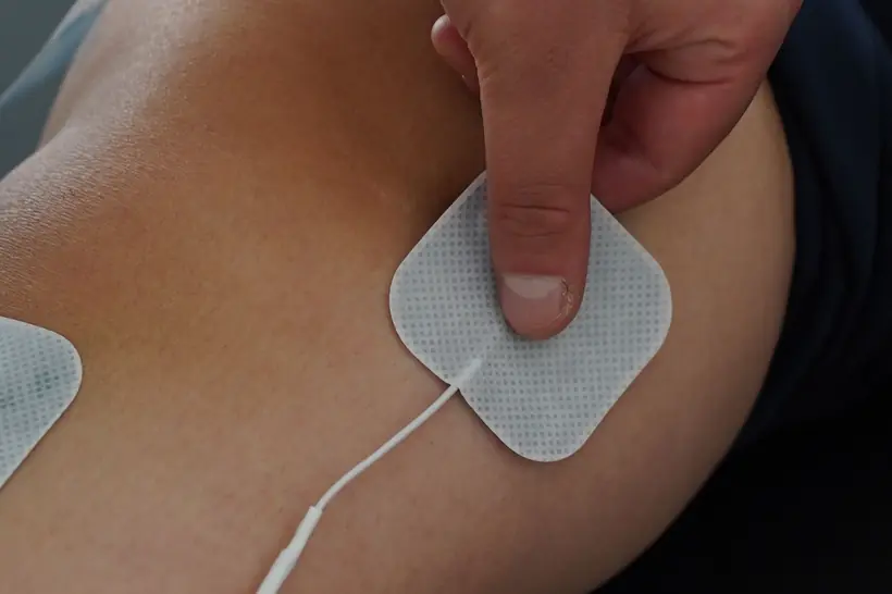 Kinesióloga colocando un electrodo sobre el hombro de un paciente