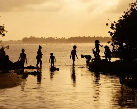 Siluetas de chicos jugando en el agua de la orilla contra el sol del atardecer